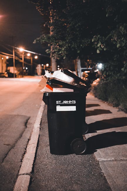 A collection of discarded rubbish is accumulated on the pavement in front of a green-painted metal fence with decorative white chalk or paint drawings of figures and abstract designs. The waste includ
